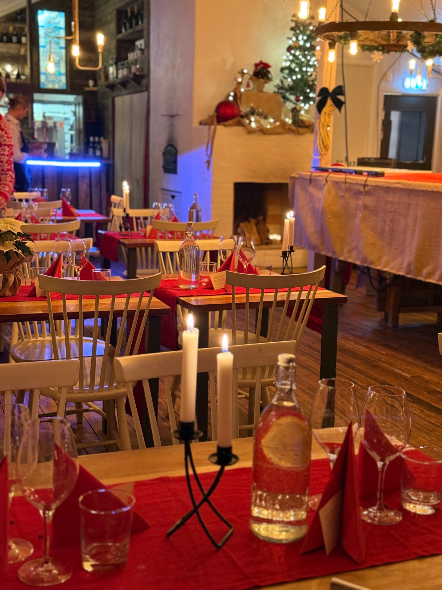 Juldukat matsal med tända ljus, röda servetter och vinglas framför brasa och gran